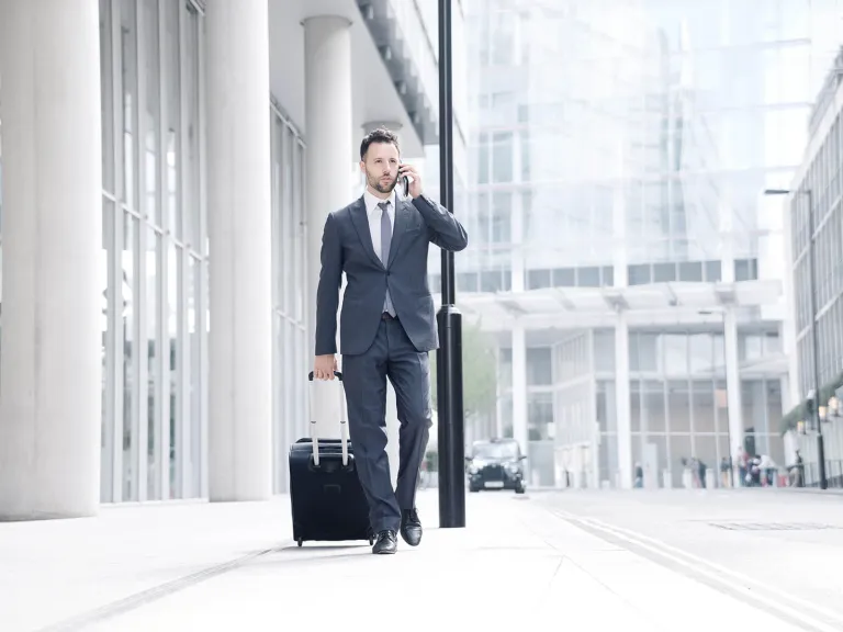 TITANIUM Mastercard Corporate Black: Un hombre hablando por teléfono mientras camina con una maleta de mano 