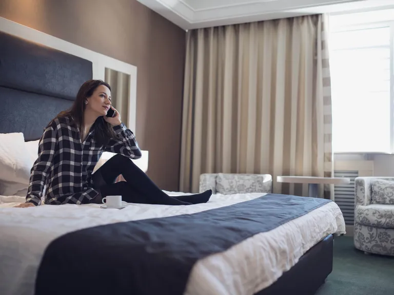 Una mujer sentada en la cama de un hotel hablando por teléfono 