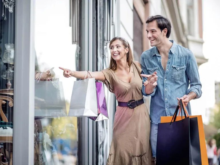 Una mujer y un hombre con sus bolsas de compras mirando un escaparate 