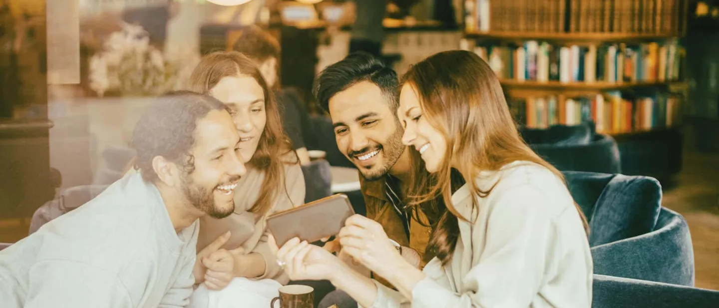 Un grupo de amigos sentados en una cafetería viendo los beneficios de tener una tarjeta adicional Diners Club