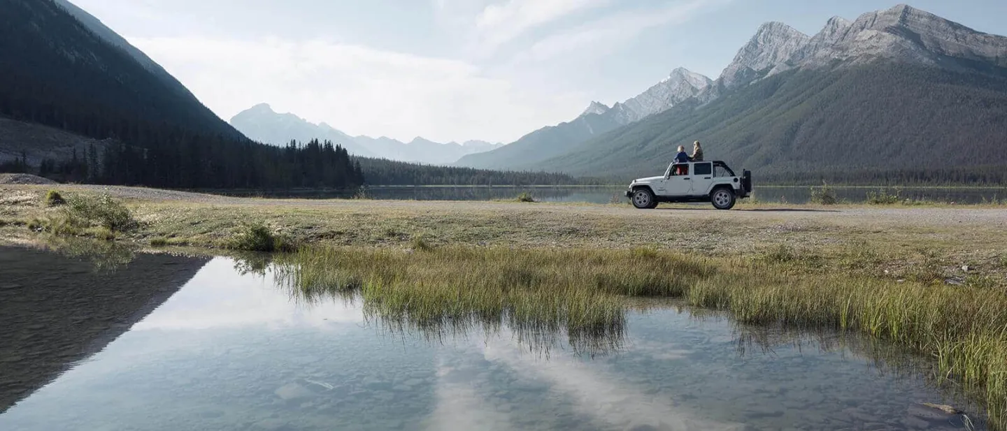 Plan de ahorros más Diners Club Miles: Un auto blanco recorriendo un paisaje de montañas y un lago 