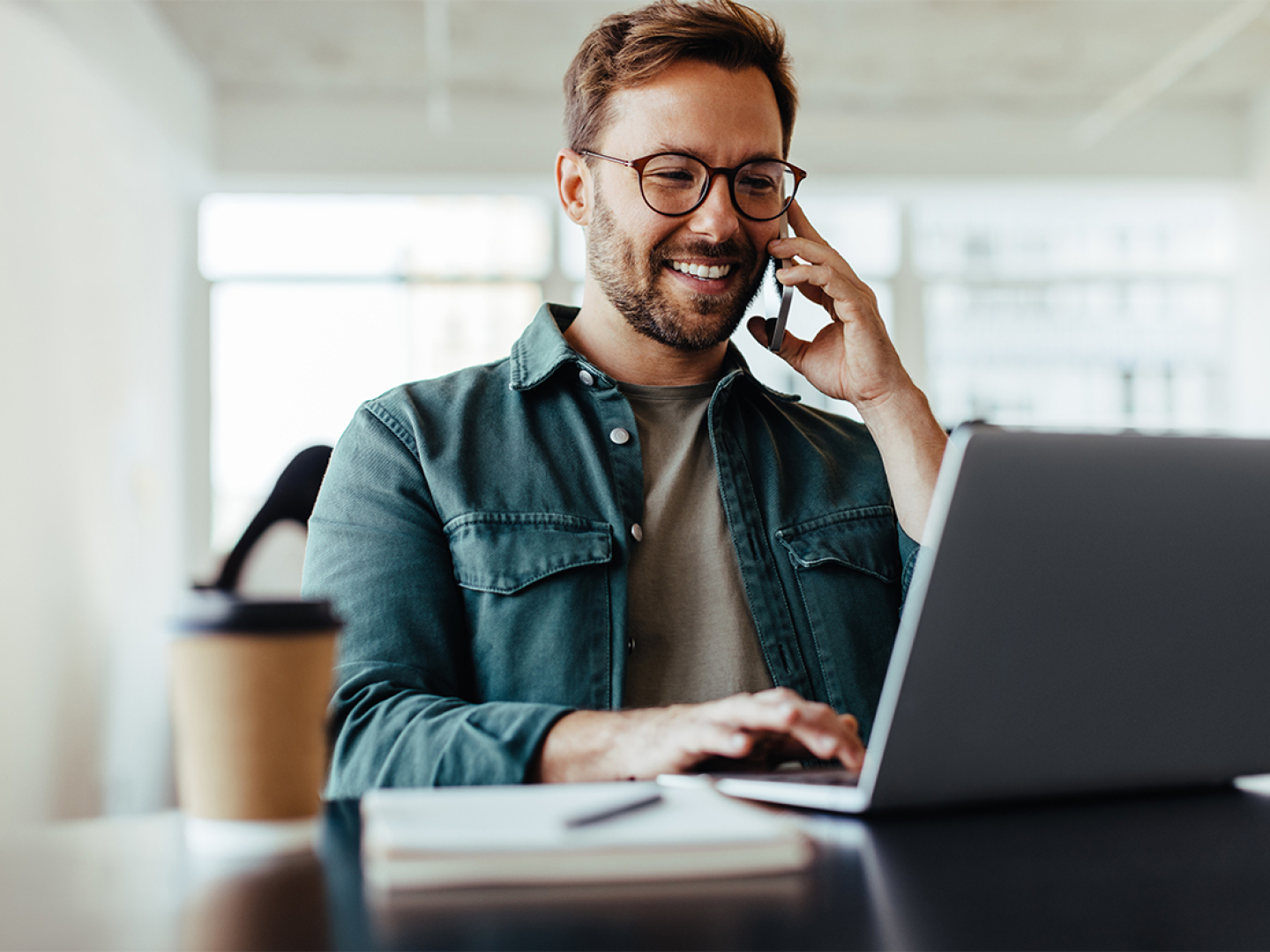 Hombre hablando por teléfono y trabajando en su computador