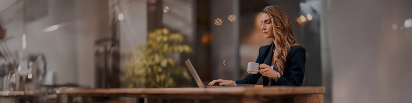 Mujer trabajando con una computadora y una taza en la mano